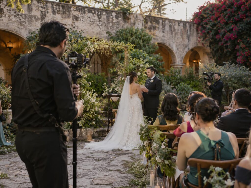 Dos videógrafos grabando la lectura de votos de los novios en una ceremonia de boda al aire libre.