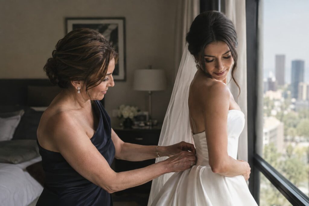 Madre de la novia ajustando el vestido de boda junto a un ventanal durante los preparativos del getting ready en un hotel de CDMX.