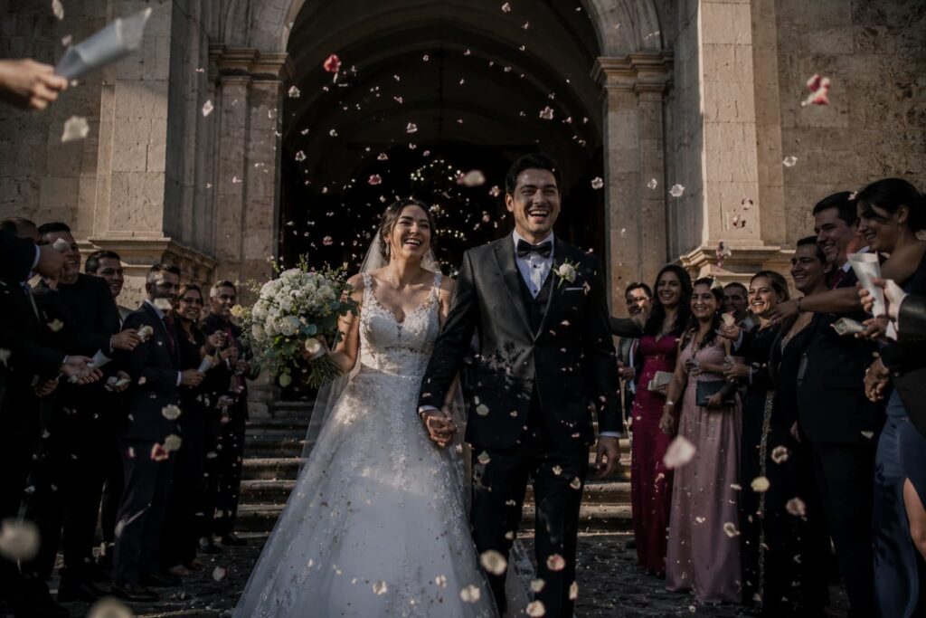 Novios saliendo de iglesia en CDMX con lluvia de pétalos durante cobertura de boda